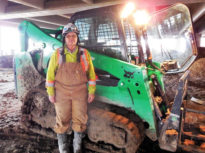 female construction worker in ppe in front of equipement