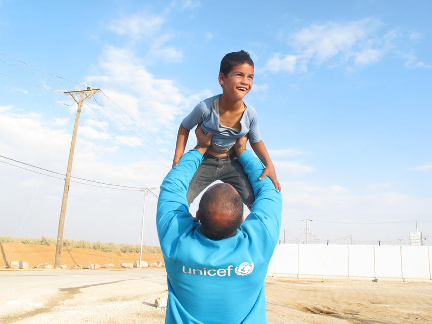 man wearing a unicef top lifting a child in the air