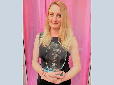 female keller employee holding glass award in front of pink background
