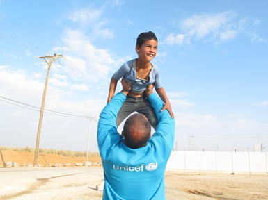 man wearing a unicef top lifting a child in the air
